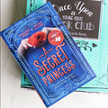 a hardcover edition of "A Secret Princess" by Margaret Stohl and Melissa de la Cruz sits on a green box