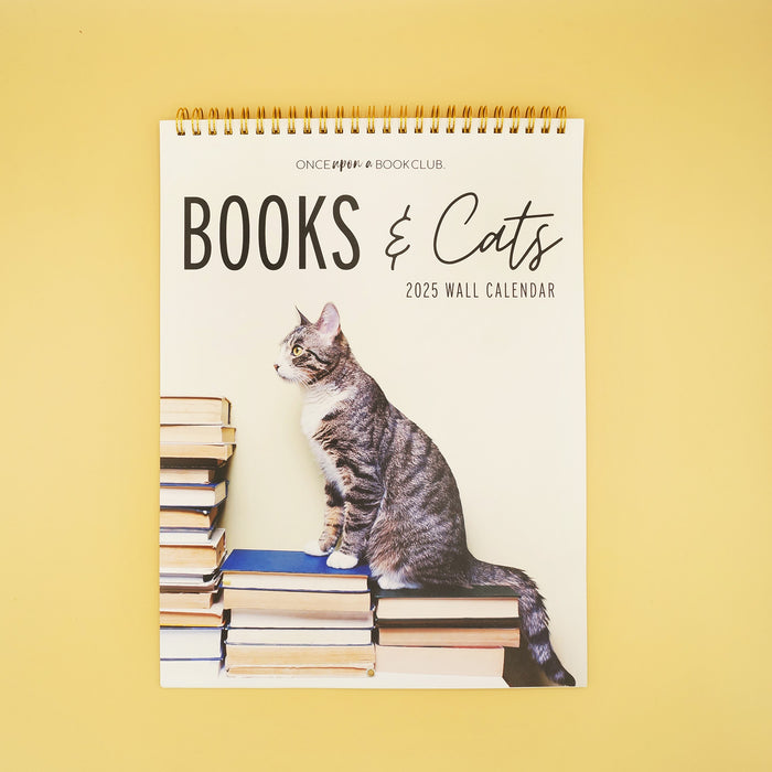 A 2025 Wall Calendar of Books & Cats. showing a gray cat on the front standing on three stacks of books