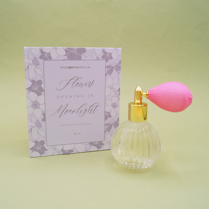 A purple box that reads "Flowers opening in Moonlight". A glass bottle with gold metalwork and a pink atomizer sits in front of the box.