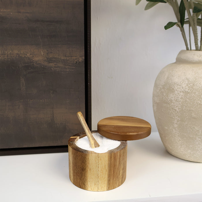 A wooden container of bath salts sits open with a wooden spoon sticking out.