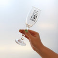 Hand holding a champagne flute that reads "May your year be as full as your TBR List" and features an etching of books along the bottom of the glass.