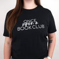A woman wearing a black short-sleeve t-shirt with the white text 'Once Upon a Book Club' printed across the chest, shown against a plain light background.