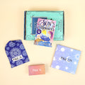 A hardcover edition of The Sun and the Starmaker lays on a green OUABC box. In front of the box are three more wrapped gifts in various patterns labeled with page numbers.