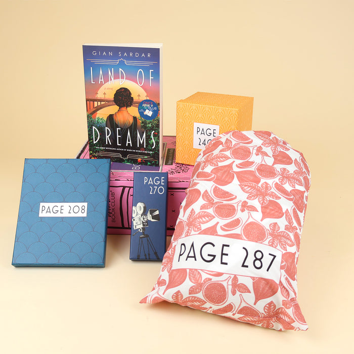 A paperback edition of Land of Dreams stands on a pink OUABC box next to a box labeled with a page number. In front of the box are three more wrapped gifts in various patterns labeled with page numbers.
