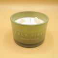 a green candle with white wax and crystals in it labeled "Good Vibes scented candle" on a yellow background