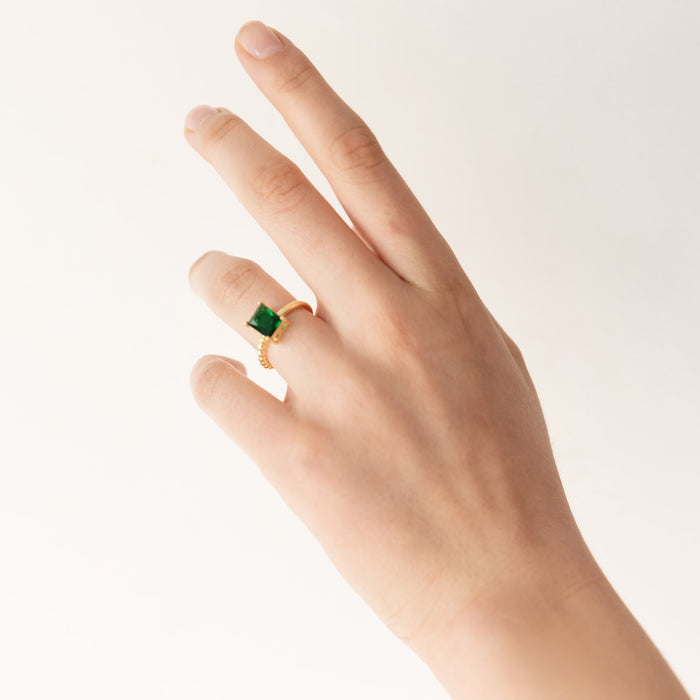 A white hand wears a green emerald ring with a gold band
