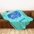 A turquoise and blue patterned throw blanket inspired by the Once Upon a Book Club Young Adult box is draped over a brown leather couch in a living room setting.